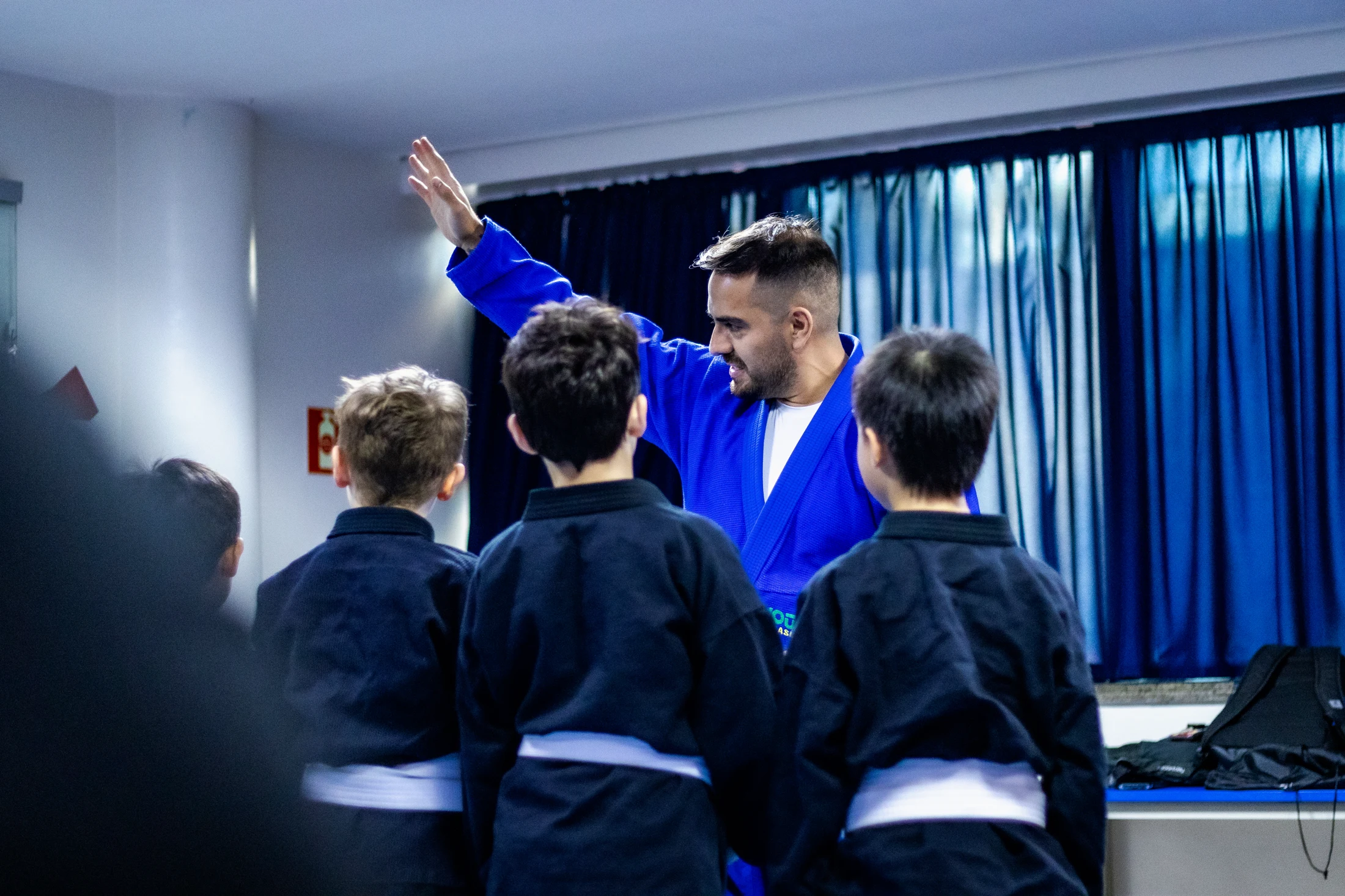 A coach in a blue gi guiding students on the mat